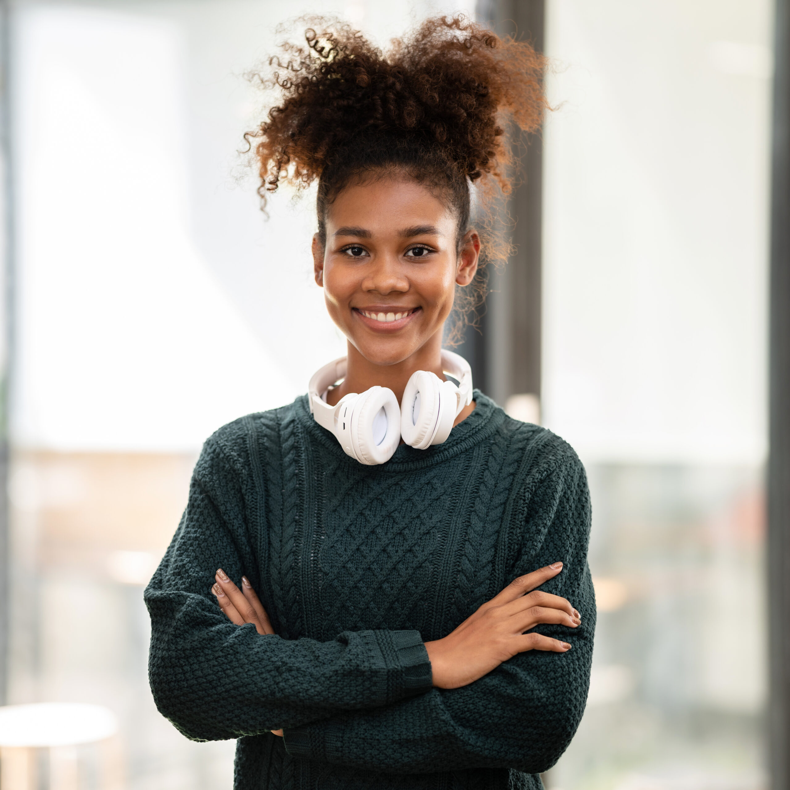 African american student woman in sweater wearing headphones around neck and standing with arms crossed after studying lesson online class while learning education and knowledge in university.